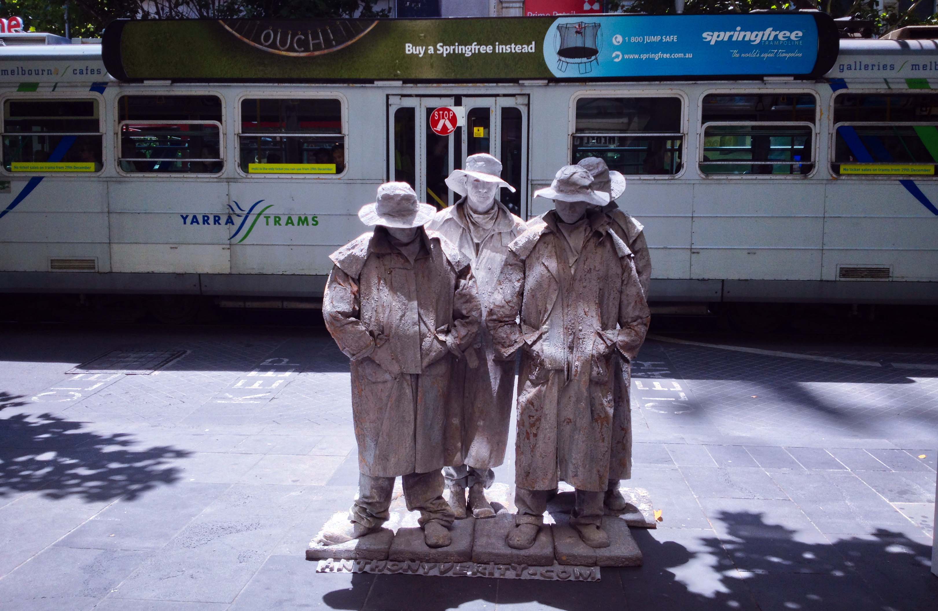 Bốn người tượng đứng trước trạm tàu điện (tram) trong một trưa hè tràn nắng trên khu phố mua sắm Bourke Street Mall. Họ đứng bất động hàng giờ, mỗi tư thế thay đổi đều giữ rất lâu.