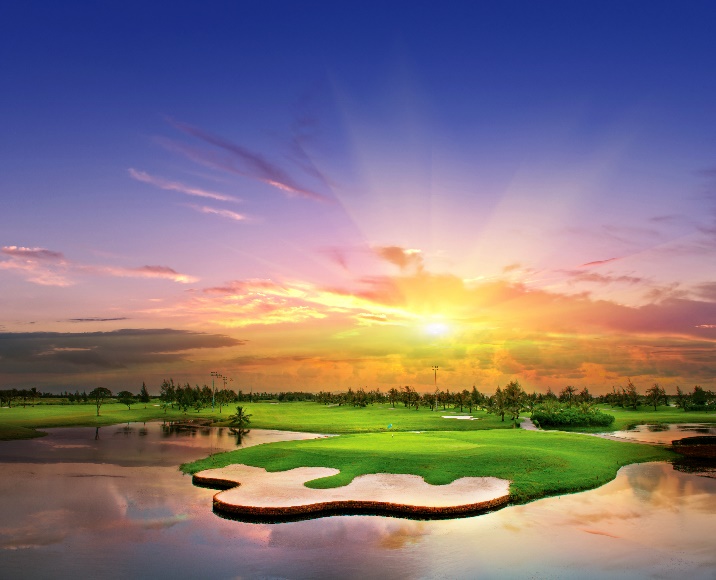 A golf course with a body of water and a sunset  Description automatically generated