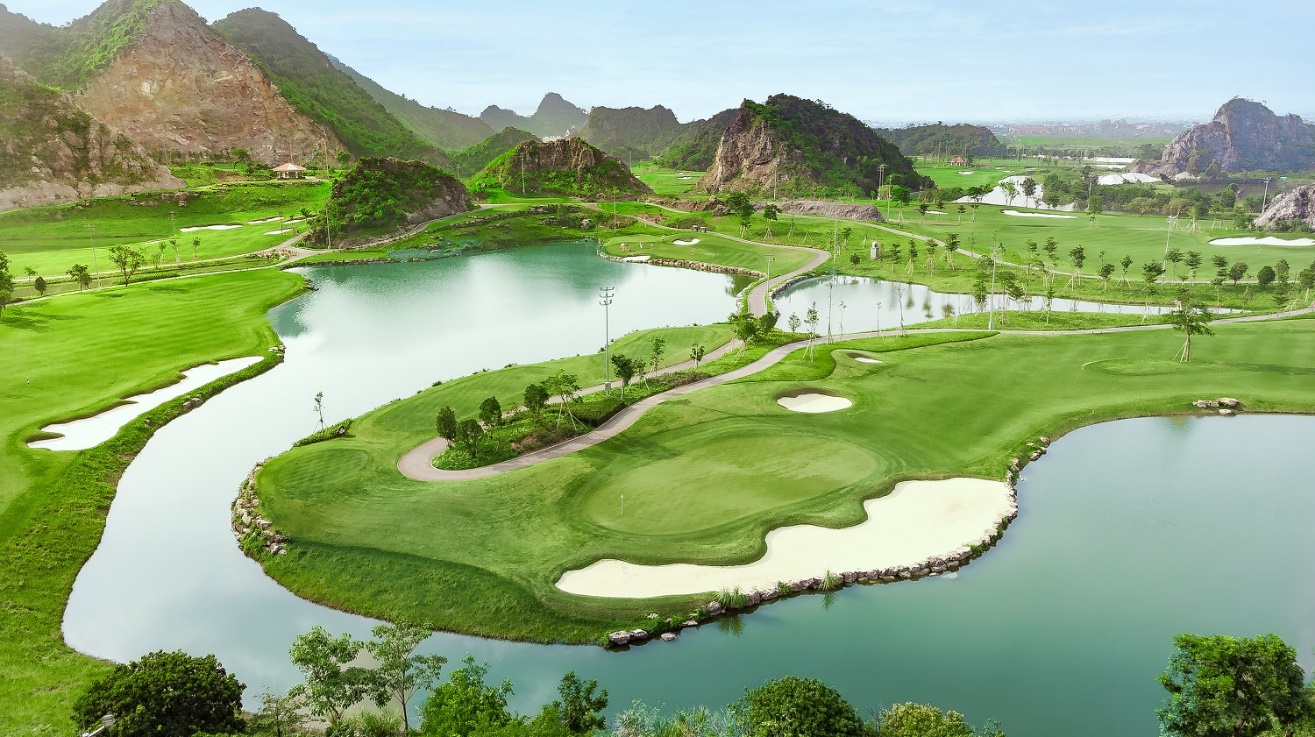 Legend Valley Country Club: Từ vùng đầm lầy hoang sơ đến "thiên đường golf" giữa lòng Ninh Bình- Ảnh 4. A golf course with a lake and mountains AI-generated content may be incorrect.