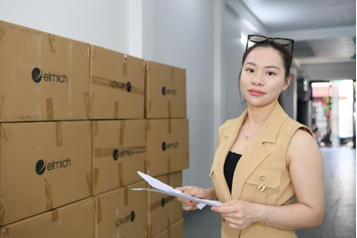 A person holding papers in front of a wall of boxes  Description automatically generated