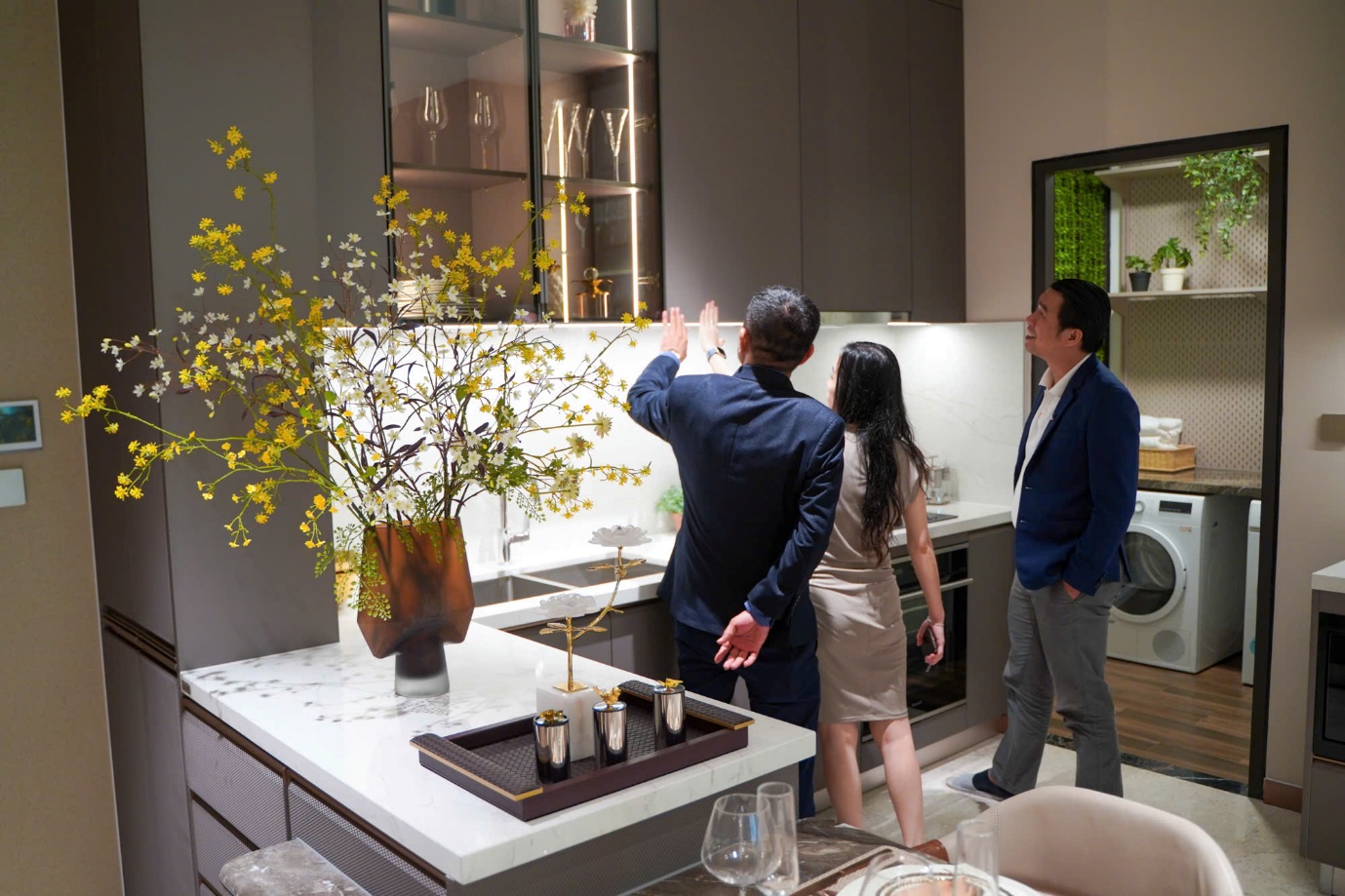 A group of people standing in a kitchen  Description automatically generated