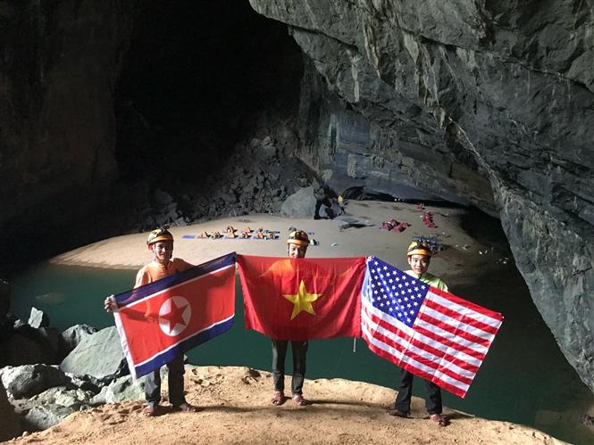 Khách du lịch khám phá hang động chụp ảnh cùng với 3 lá Quốc kỳ Mỹ - Triều Tiên – Việt Nam tại hang Én, tỉnh Quảng Bình. ẢNh: TTXVN