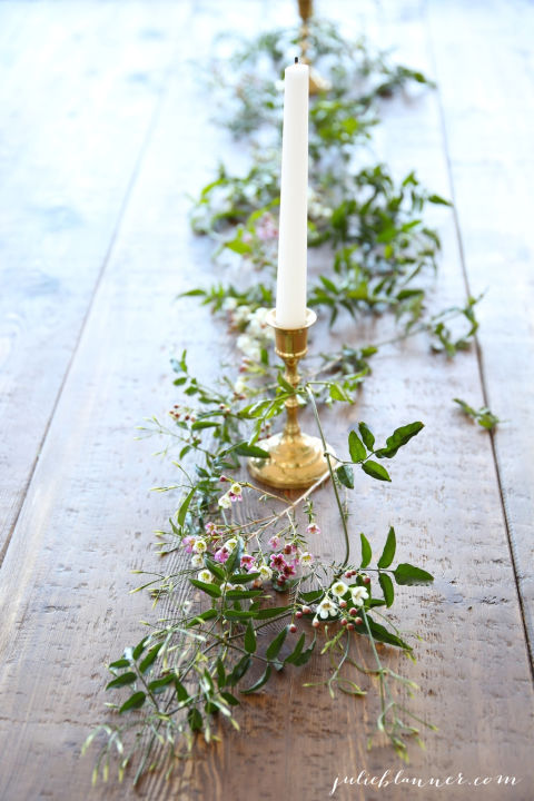 3. Trang trí trên mặt bàn gỗ với những nhánh hoa với phần đa là lá xanh cùng với cây nến trắng.
