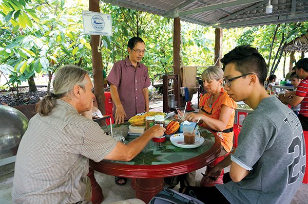 Chủ của một homestay kết hợp điểm tham quan ở Cần Thơ (người đứng) đang trò chuyện với khách du lịch. Ảnh: Đào Loan