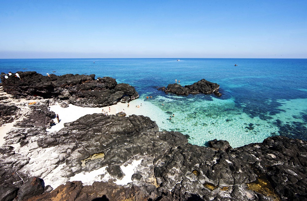 Bãi tắm ở đảo Bé cát trắng mịn, nằm giữa những cánh cung vách đá trầm tích núi lửa hàng triệu năm cao sừng sững.