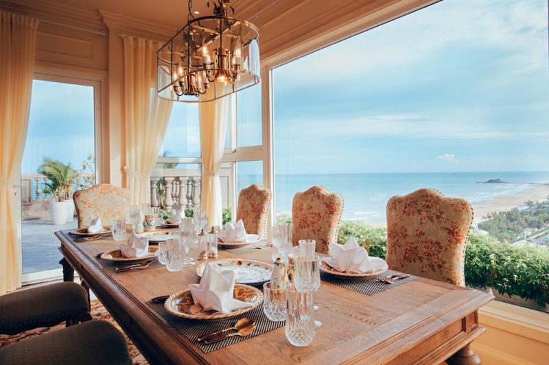 Phòng ăn thoáng đãng với cửa sổ lớn nhìn ra biển. Bộ bàn ghế đồng gam màu vàng hợp tông với tổng thể căn hộ.