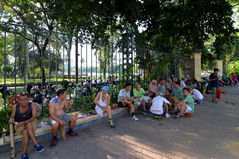 Những người cao tuổi tụ tập dưới bóng râm xung quanh hàng rào công viên Thống Nhất sau khi đi tập về.