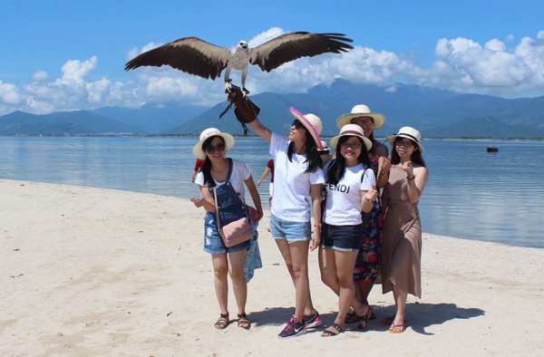 Nhóm du khách chụp hình với những chú chim được các bạn trẻ ở Khánh Hòa thuần nuôi, đưa ra Điệp Sơn cho khách thuê chụp hình.