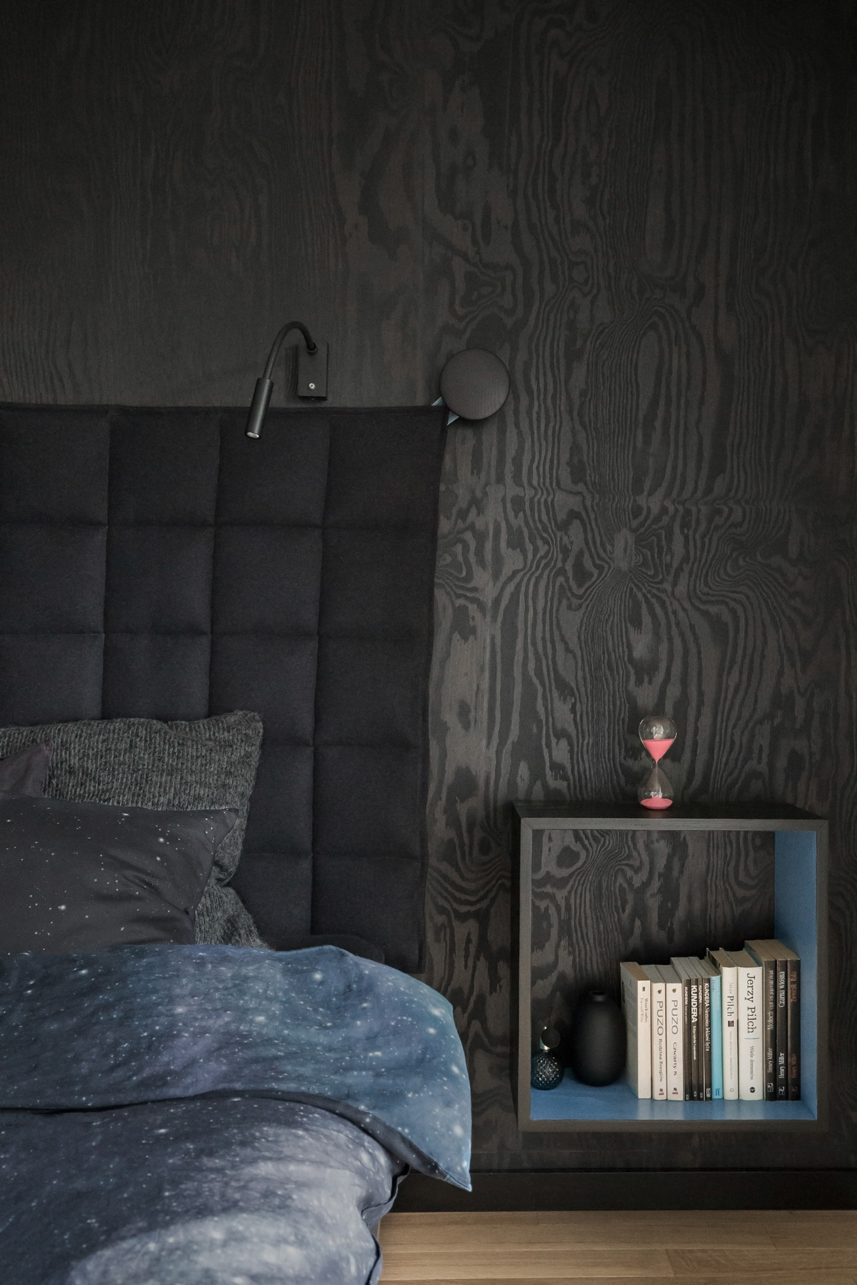 Một chiếc đèn treo tường hiện đại cũng có màu đen được treo ở mỗi bên của đầu giường để chiếc kệ bên cạnh đầu giường có không gian đặt những thứ khác. Các chi tiết màu xanh được điểm xuyết khéo léo tạo nên một vệt sáng cho căn phòng.