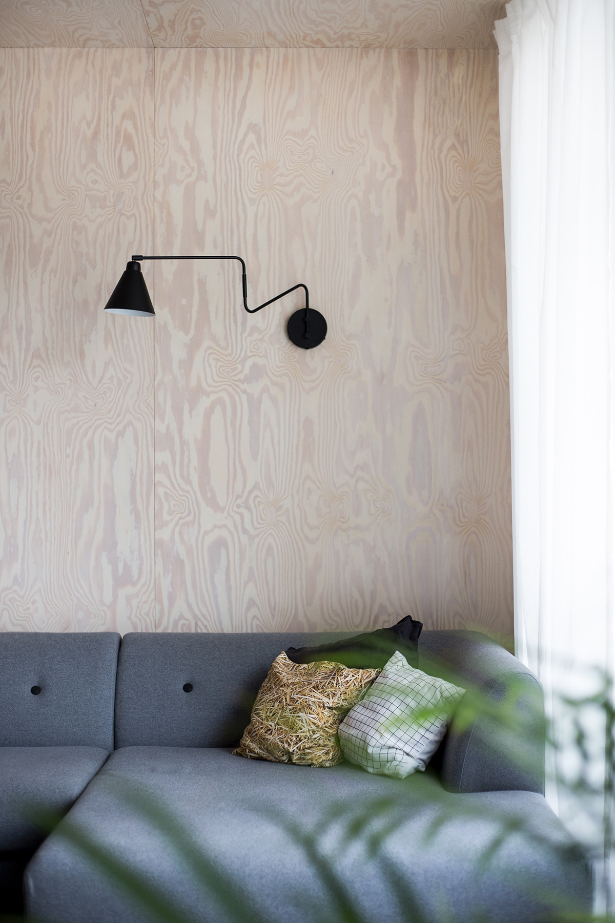 Một chiếc đèn tường màu đen với thiết kế ấn tượng trở thành điểm nhấn cho bức tường gỗ màu sáng. Chiếc đèn đảm nhận vai trò cung cấp ánh sáng cho khu vực ghế sofa.