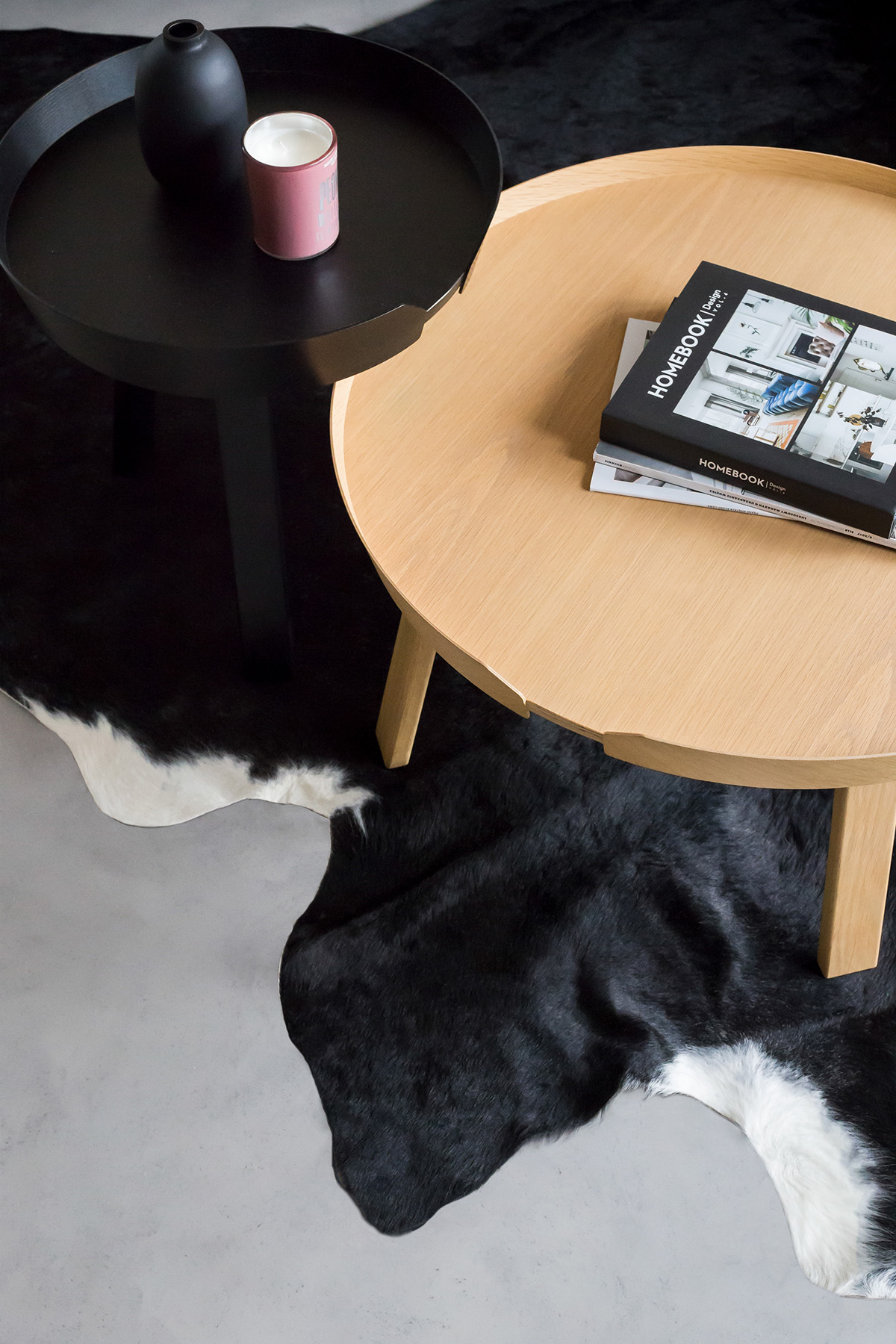 Bộ bàn cafe tròn đặt trên một tấm thảm giả lông động vật màu đen và trắng hoàn toàn hòa hợp với không gian tổng thể của phòng khách. Chiếc cốc nến trang trí đặt trên bàn là điểm nhấn màu hồng đầu tiên của ngôi nhà.