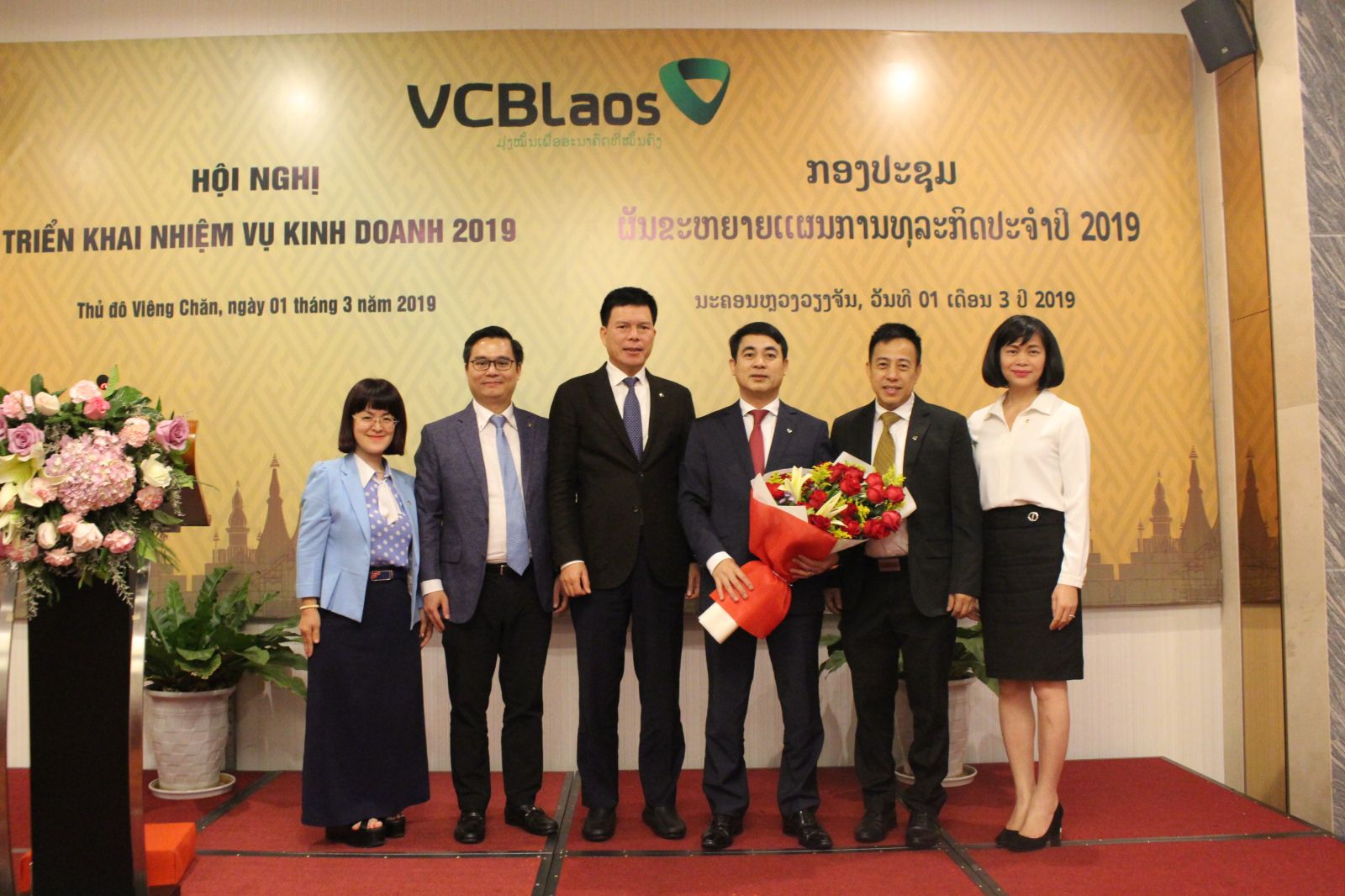 Ông Phạm Mạnh Thắng – Phó Tổng Giám đốc Vietcombank, Chủ tịch HĐQT Vietcombank Lào (thứ 3 từ trái sang) cùng các thành viên HĐQT Vietcombank Lào tặng bó hoa tươi thắm cho ông Nghiêm Xuân Thành - Chủ tịch HĐQT Vietcombank (thứ 3 từ phải sang), bày tỏ cảm ơn đối với sự quan tâm, sát sao của Ban Lãnh đạo Vietcombank dành cho hoạt động của Vietcombank Lào