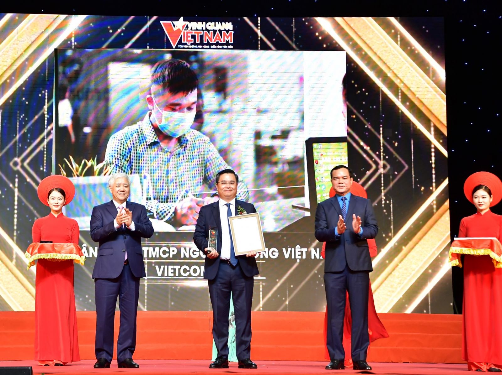 Chủ tịch UBTW MTTQ Việt Nam Đỗ Văn Chiến (bên trái) trao Biểu trưng và Chủ tịch Tổng LĐLĐ Việt Nam Nguyễn Đình Khang (bên phải) trao Chứng nhận vinh danh cho ông Nguyễn Thanh Tùng - Tổng giám đốc đại diện tập thể Vietcombank.
