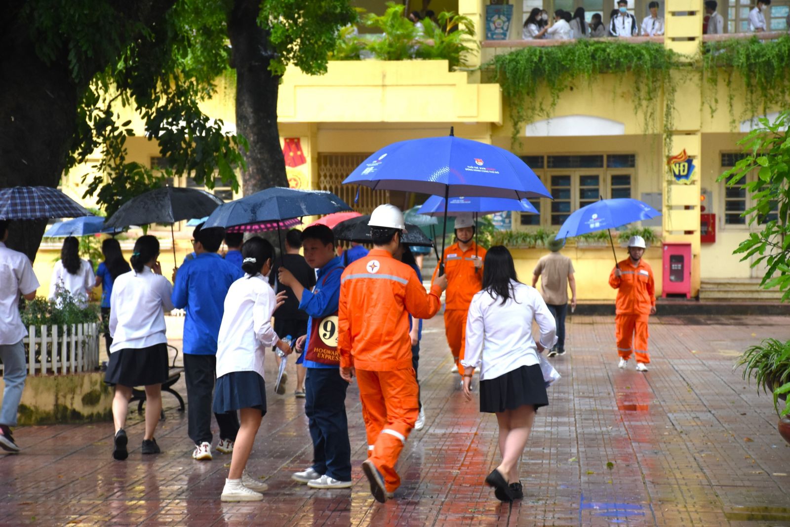 Những tình nguyện viên áo cam sẵn sàng hỗ trợ thí sinh di chuyển vào trường dưới cơn mưa.